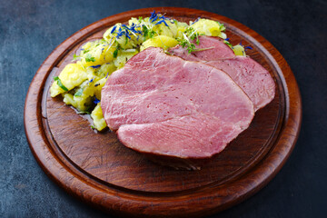 Traditionell geschmorte badisches Schäufele Scheibe serviert mit Kartoffelsalat als close-up auf einem rustikalen Holz Schneidebrett mit Textfreiraum 