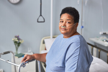 Minimal portrait of black senior woman looking at camera in hospital room with oxygen support, copy...