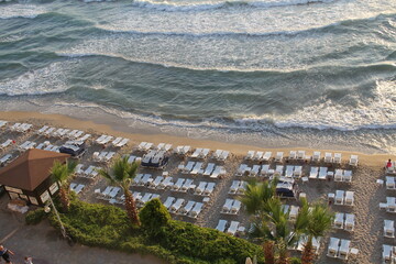 Aerial view of rows of white chaise lounges by a wavy blue sea in Turkey