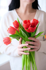 International Womens Day.Close-up of a woman in a white sweater with a bouquet of red tulips