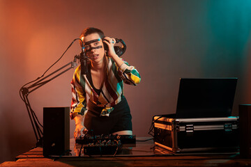 Cheerful artist mixing music at dj turntables, playing techno sounds with mixer and bass key in...