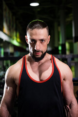 Fototapeta na wymiar A handsome muscular male bodybuilder with a beard in a black T-shirt looks at the camera in the gym