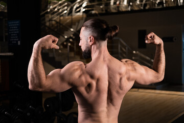 Fototapeta na wymiar A handsome muscular male bodybuilder with a pumped-up body poses and shows his back