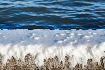 Ice crust from frozen water on parapet on embankment near the sea on clear day