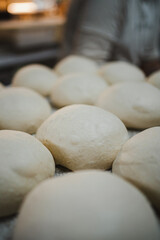 Close up view of several balls of shaped bread dough in a row. They are resting.