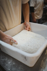 Baker folding bread dough in plastic container.