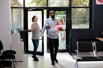 African american father holding unconscious daughter in arms after fainting while bringing little girl in hospital waiting area trying to ask for help. Health care service and concept
