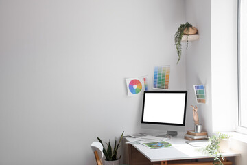 Designer's workplace with computer and tablet near light wall
