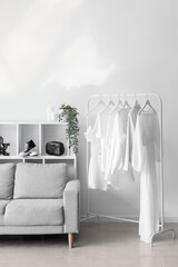 Interior of light dressing room with sofa, shelving unit and clothes