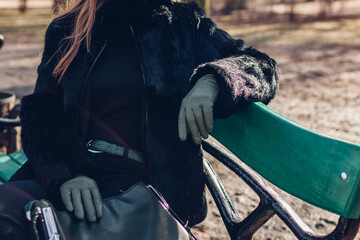 Close up of stylish leather accessories. Woman wearing green gloves and fur coat outdoors holding...