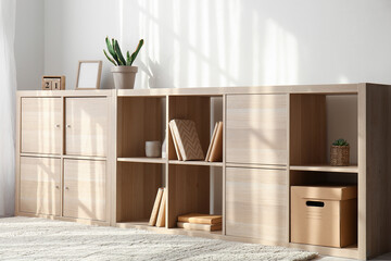 Wooden chest of drawers with books and decor near light wall