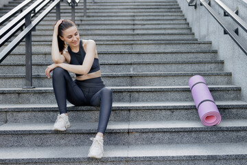 Cheerful woman in activewear relaxing after yoga classes on concrete steps.