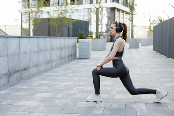 Focused sportswoman with headphones doing lunges, while training outdoors.