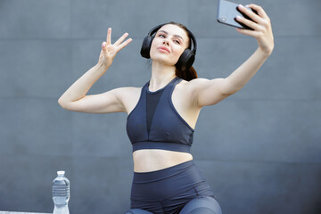 Beautiful sportswoman in headphones posing, taking selfie with smartphone.