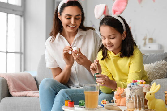 Little girl and her mother in bunny ears painting Easter eggs at home