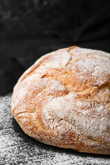 Delicious loaf of fresh bread and flour on black table