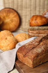 Cutting board with loaf of rye bread and delicious buns on napkin, closeup