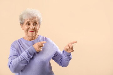 Senior woman in lilac sweater pointing at something on beige background