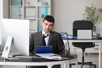 Tired young accountant working at table in office