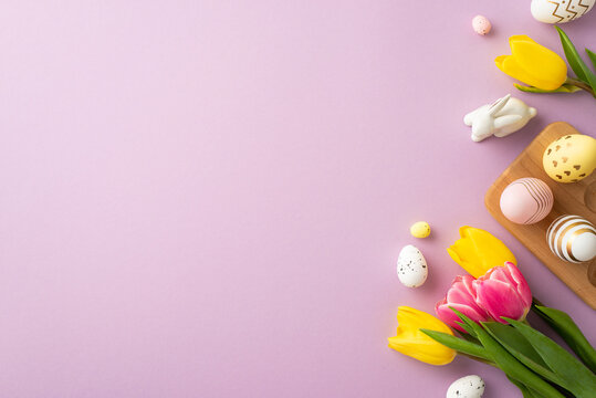 Easter celebration concept. Top view photo of colorful easter eggs in wooden holder ceramic rabbits yellow and pink tulips on isolated pastel purple background with blank space
