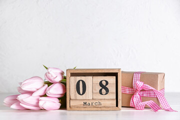 Cube calendar with date MARCH 8, gift box and beautiful tulip flowers on table near white wall. Women's Day celebration