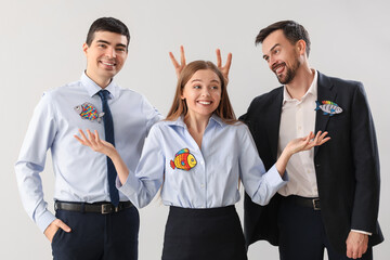 Business colleagues with paper fishes on light background. April Fools' Day celebration