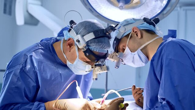 Pair of neurosurgeons bent over the patient using tools in the surgery. Doctors wear special device glasses cooperating at procedure.
