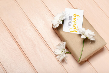 Gift box, chamomile flowers and card with text WELCOME SPRING on color wooden background