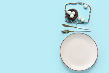 Table setting with cutlery and Easter eggs in nest on blue background