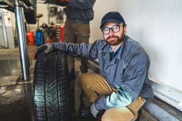 Fototapeta na wymiar Mechanic squatting with one hand on a black car tyre. Posing for a picture. Repair shop concept. High quality photo