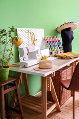 Tailor's workplace with laptop, sewing machine and organizers near green wall in workshop