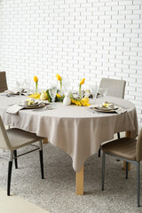 Festive dining table served for Easter celebration near white brick wall