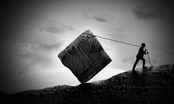 Surreal scene Of Young Businessman Pulling A Rock Block up to Hill. Sisyphus Concept. The Exhausted man pull hardly the struggle. 