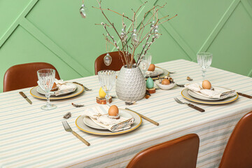 Festive dining table with eggs and pussy willow branches served for Easter celebration near green wall