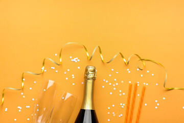 Composition with bottle of champagne, glasses, straws and serpentine on orange background