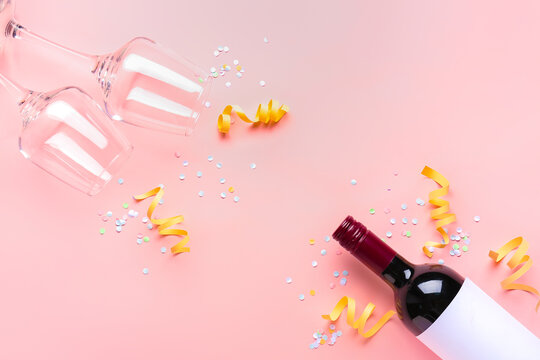 Bottle of wine, glasses, serpentine and sequins on pink background