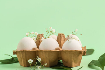 Package with Easter eggs, gypsophila flowers and plant leaves on green background