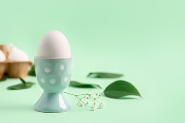 Easter egg in holder and gypsophila flowers on green background