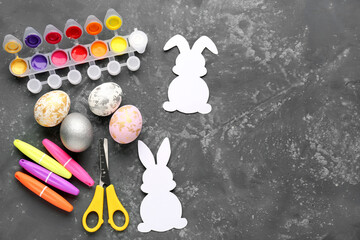 Paper rabbits with Easter eggs, scissors, markers and paints on dark background