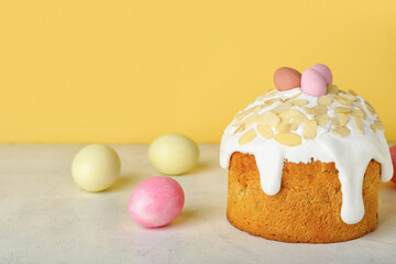 Easter cake and painted eggs on table near yellow wall