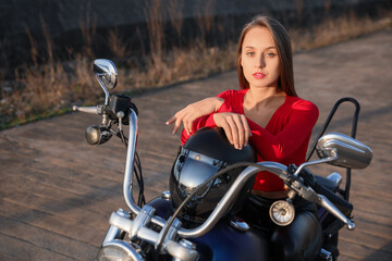Beautiful young woman with helmet sitting on motorcycle outdoors