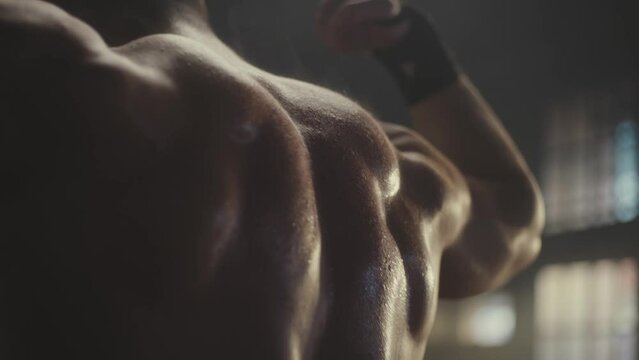 Strong muscular man posing and displaying his back muscles on camera while standing at gym. Shooting in slow-motion