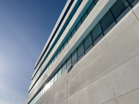 The exterior wall of a contemporary commercial style building with concrete prefabricated panels and glass windows. The futuristic building has engineered cement cladding frame panels. 