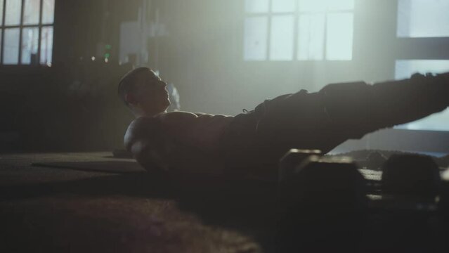 A man with strong six pack muscle lying down on floor doing abdominal exercise, leg raise reverse crunch in the gym. Low angle camera view