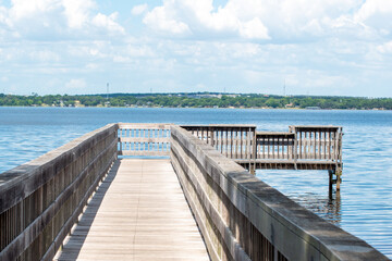 A wooden plank wharf or pier with wood rails jutted into the still blue ocean water.  The blue sky...