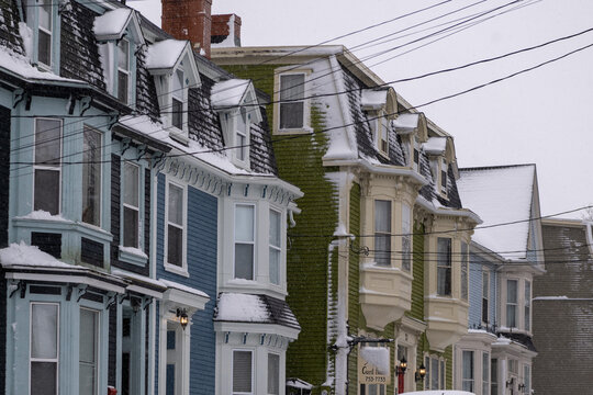 St. John's, NL, Canada - February 2023: A row of multiple colorful wooden vintage row houses, townhouses, and Victorian style painted buildings. The view is of the street with a cloudy blue sky.