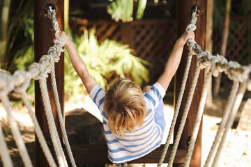 Preschool child playing on rope swing in beautiful tropical kindergarten yard.