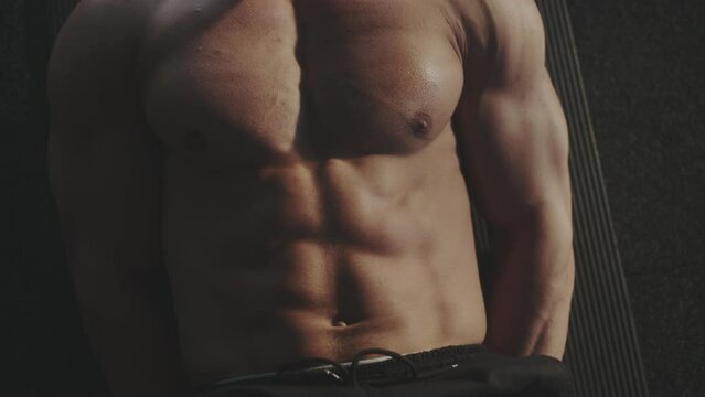 Body bulder man training and doing physical exercise while laying on yoga mat, lifting legs to stretch muscles