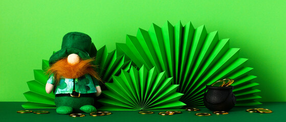 St Patrick's Day leprechaun, decorative paper fans, pot of gold on green table.