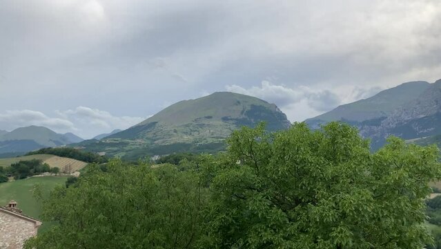 Enchanting panorama from Montefortino with the momentous Sibillini mountains promptly on display in a not so distant background under an unreal sky and hazy central sun with vivid greenery all around